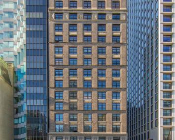 A 20-story Manhattan building made of grey stone and small-ish windows.