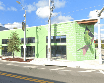 An empty lime green building sits on an empty intersection surrounded by blue skies with a few clouds.