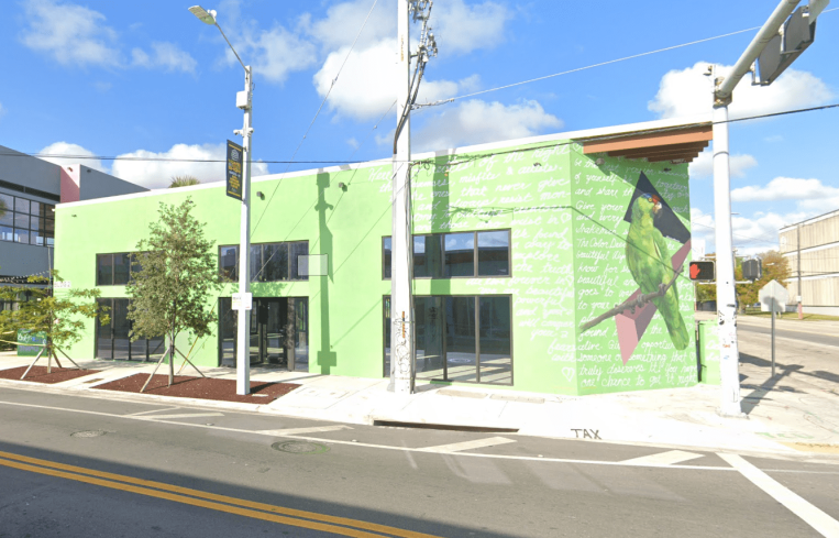 An empty lime green building sits on an empty intersection surrounded by blue skies with a few clouds.