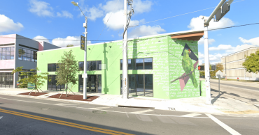 An empty lime green building sits on an empty intersection surrounded by blue skies with a few clouds.