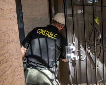 A man in a vest that says "constable" knocking on a door.