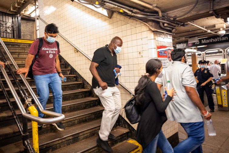 People in masks walking down subway steps.