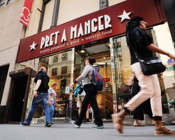 People walking by a restaurant on a sidewalk.