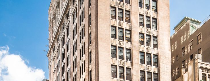 A large white building the the Flatiron District of Manhattan across a backdrop of a blue sky.