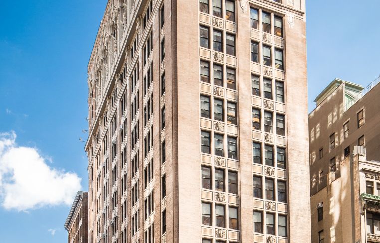 A large white building the the Flatiron District of Manhattan across a backdrop of a blue sky.