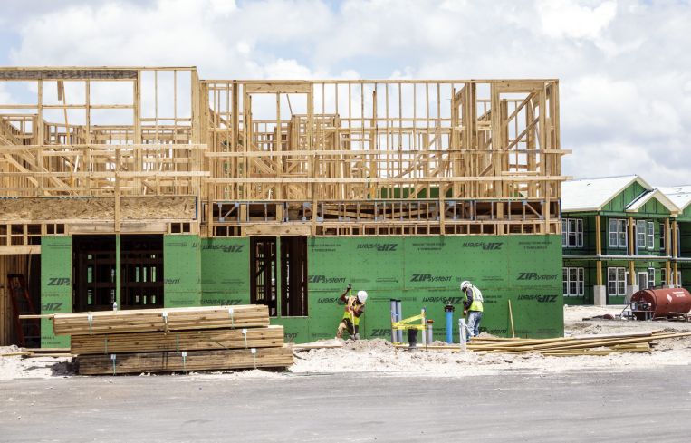 Construction workers beneath a large wood frame of a building.