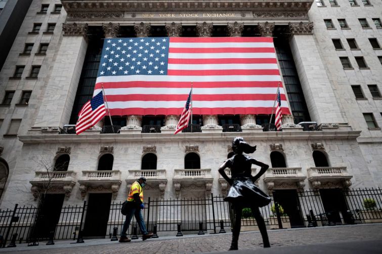 A small bronze statue of a girl stands and faces the New York Stock Exchange, draped in an American flag.