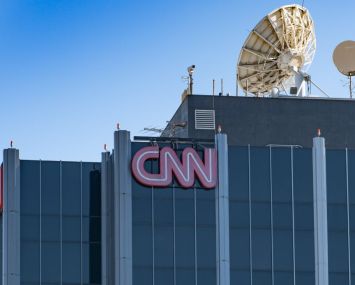 A large grey skyscraper with the red CNN logo on its top with a satellite dish on the roof.