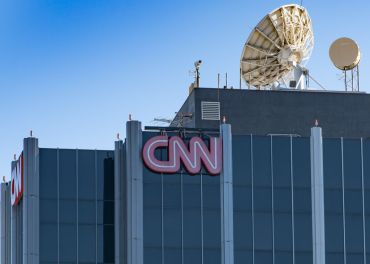 A large grey skyscraper with the red CNN logo on its top with a satellite dish on the roof.