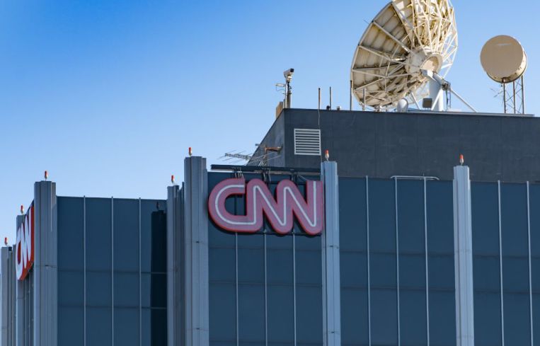 A large grey skyscraper with the red CNN logo on its top with a satellite dish on the roof.