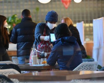 A masked waitress delivers food to a woman with her back to the camera at Hudson Yards.