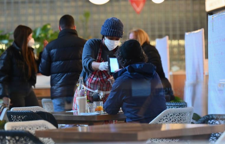 A masked waitress delivers food to a woman with her back to the camera at Hudson Yards.
