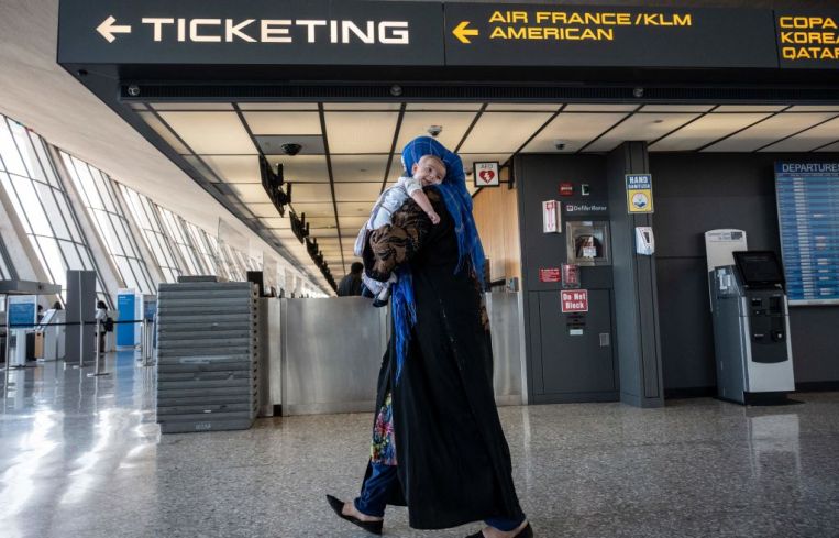 A woman walks with a baby on her arm in an airport.