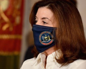 New York Governor Kathy Hochul wears a mask and looks towards the left.