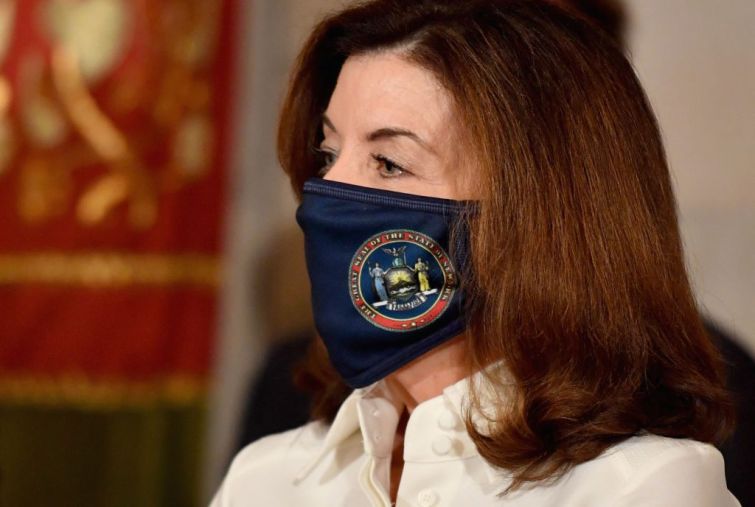 New York Governor Kathy Hochul wears a mask and looks towards the left.