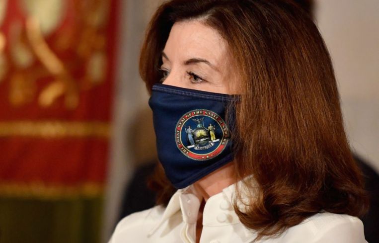 New York Governor Kathy Hochul wears a mask and looks towards the left.