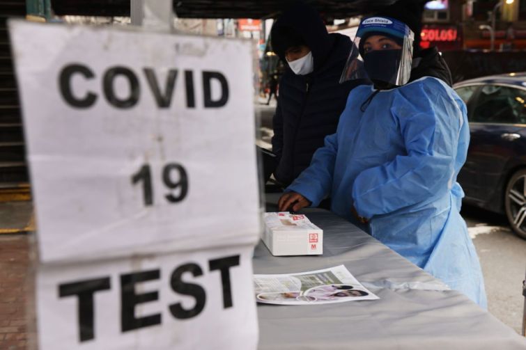 A sign saying "COVID 19 TEST" in front of a healthcare worker adorned in a face shield and blue suit.