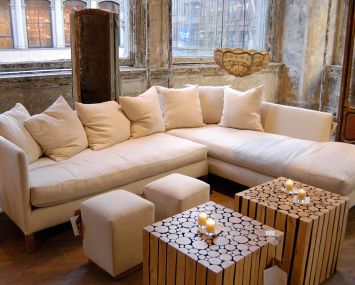 A white couch with fluffy pillows centered in a photo with wooden tables and candles on top.