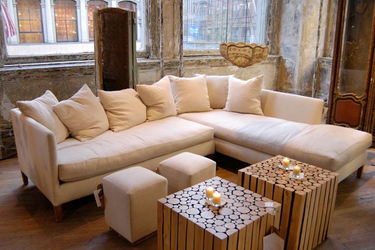 A white couch with fluffy pillows centered in a photo with wooden tables and candles on top.