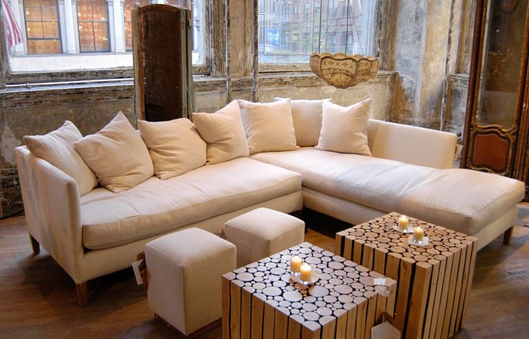 A white couch with fluffy pillows centered in a photo with wooden tables and candles on top.