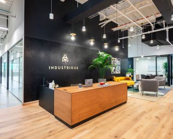 A modern office with black walls and Industrious' logo printed on the back wall behind a front desk.