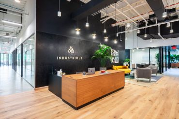 A modern office with black walls and Industrious' logo printed on the back wall behind a front desk.