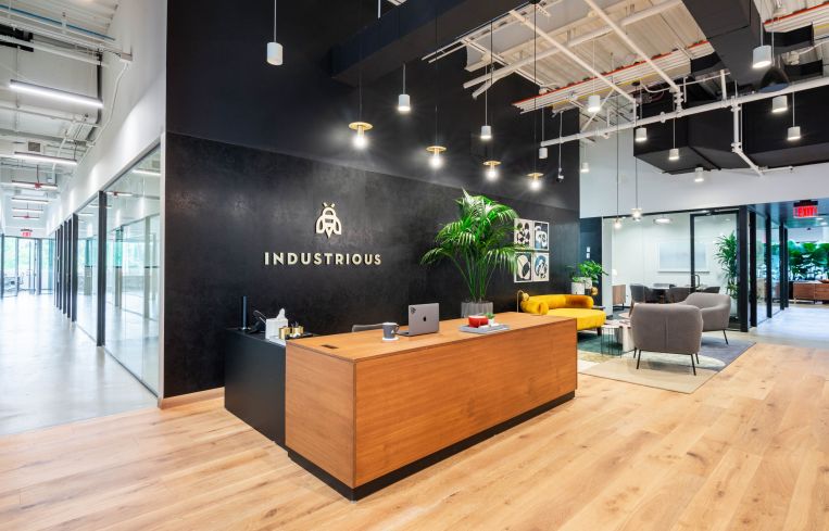 A modern office with black walls and Industrious' logo printed on the back wall behind a front desk.