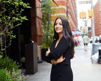 A woman standing on a sidewalk and smiling.