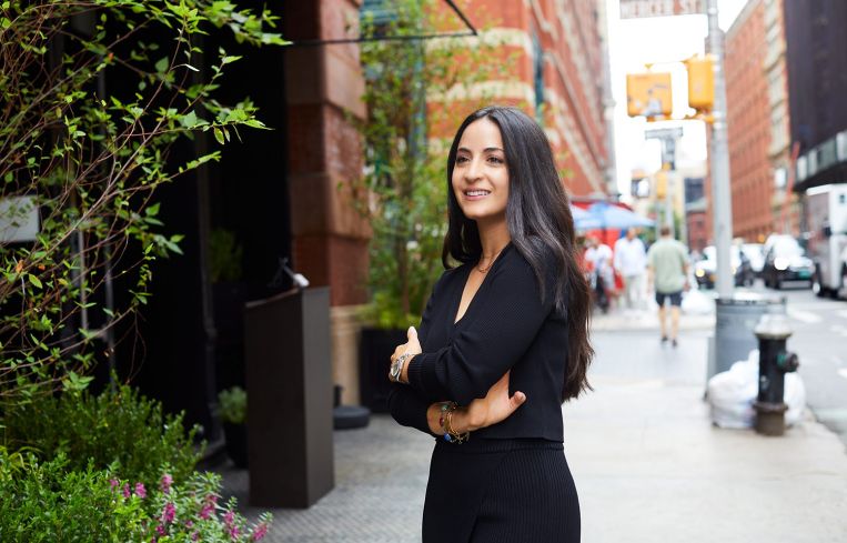 A woman standing on a sidewalk and smiling.