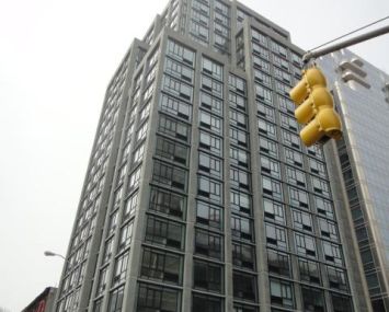 A large grey building with a yellow traffic light in front of it backed by a white blank sky.