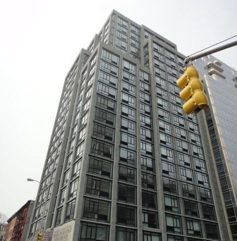 A large grey building with a yellow traffic light in front of it backed by a white blank sky.