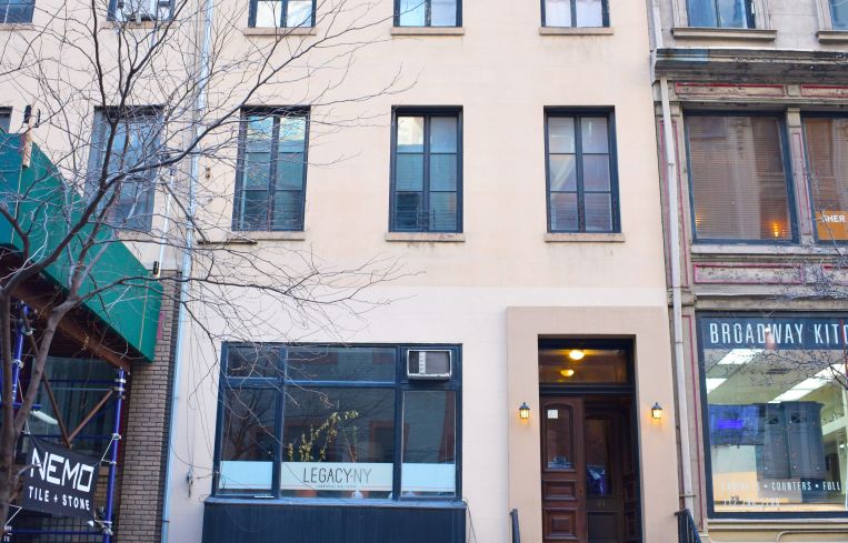 A five-story white apartment building with a green awning and tree in front of tit.