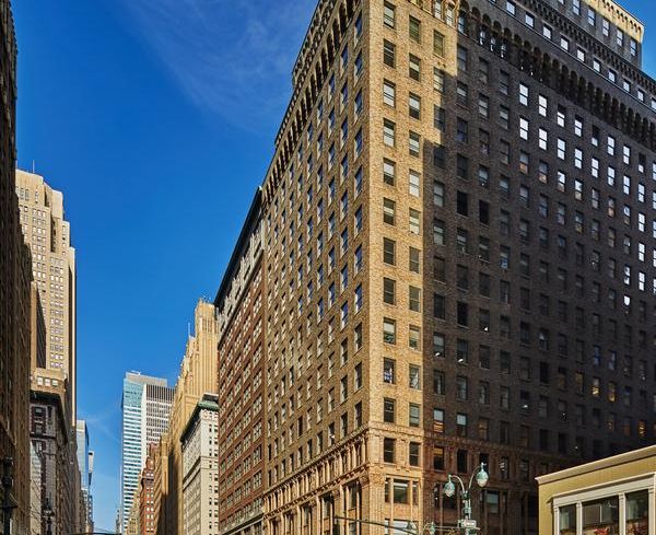 A large off-white building towers in New York City with yellow cabs in front of it.