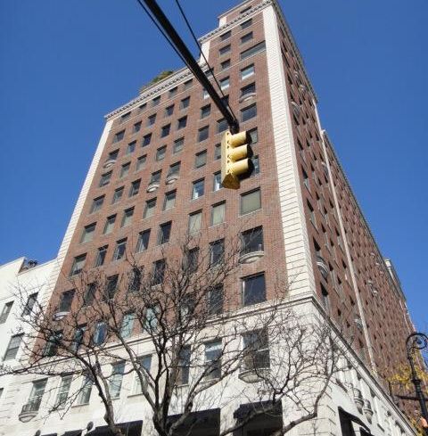 A large brown building with a traffic light in the foreground in front of it.