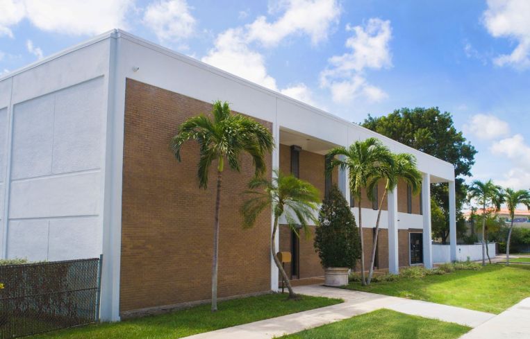 A brown brick and white painted building with palm trees in front of it.