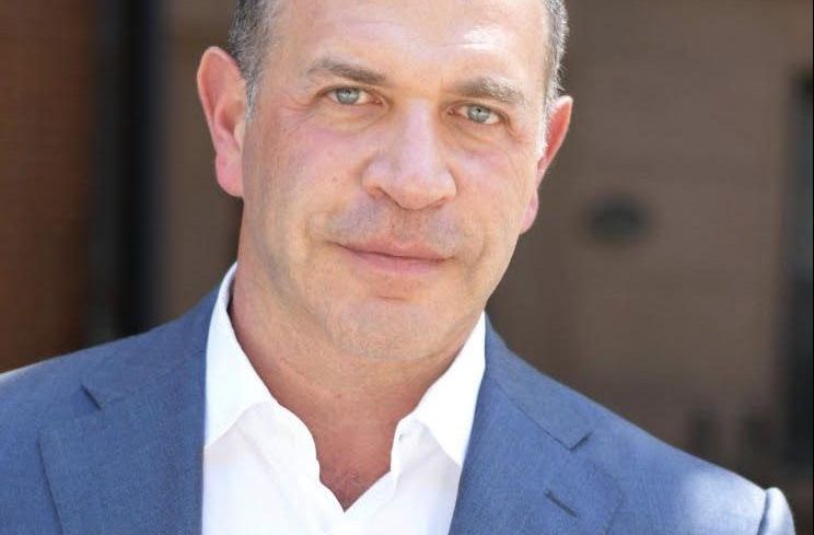 A man in a blue suit backed by a red building.