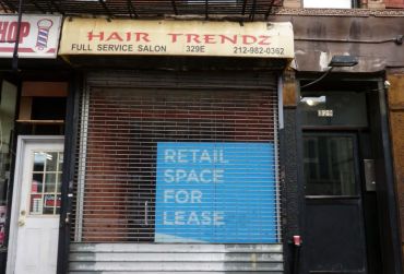 A blue "Retail Space for Lease" sign sits in a gated storefront formerly belonging to Hair Trendz.