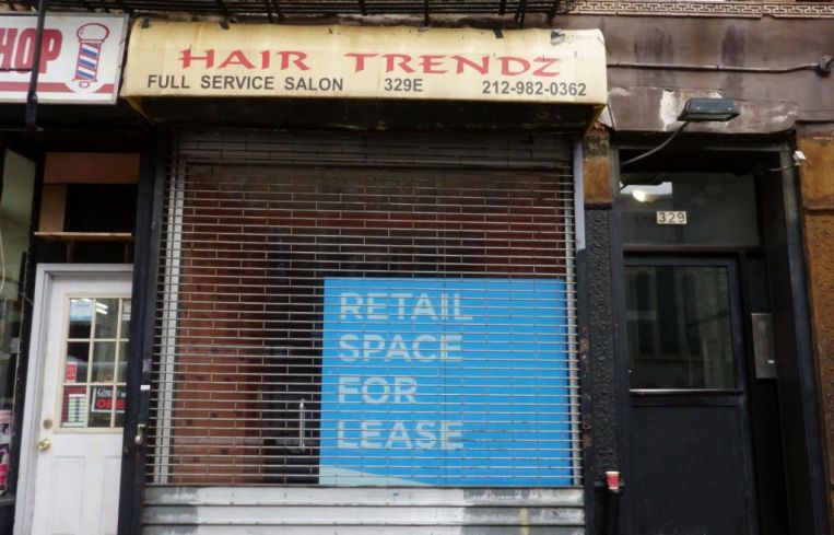 A blue "Retail Space for Lease" sign sits in a gated storefront formerly belonging to Hair Trendz.