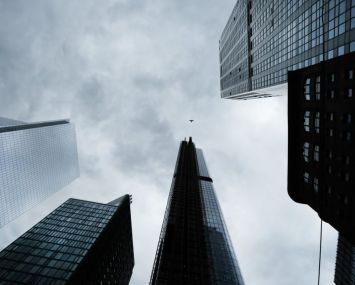An upwards view towards the tops of several skyscrapers in New York City backed by a cloudy grey sky.