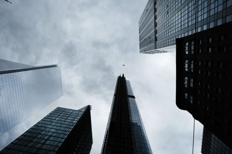 An upwards view towards the tops of several skyscrapers in New York City backed by a cloudy grey sky.