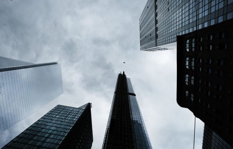 An upwards view towards the tops of several skyscrapers in New York City backed by a cloudy grey sky.