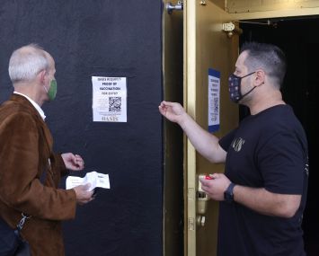 A doorman at Oasis informs a customer that a vaccination card is required to enter the club.