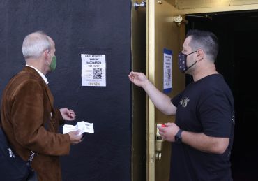 A doorman at Oasis informs a customer that a vaccination card is required to enter the club.