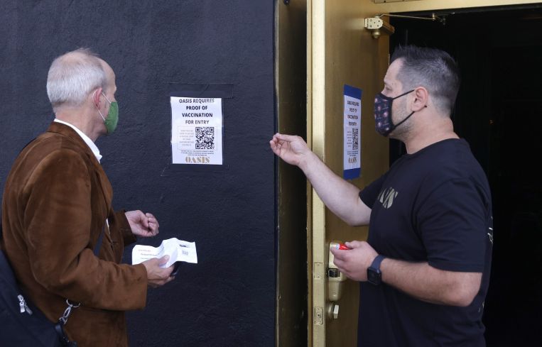 A doorman at Oasis informs a customer that a vaccination card is required to enter the club.