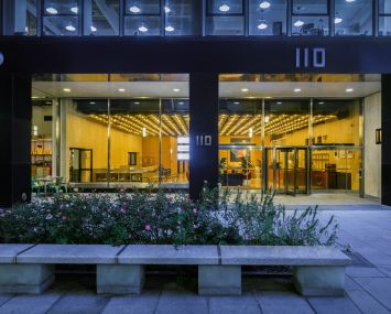 A window shows a yellow-lit building's lobby with plant life outside.