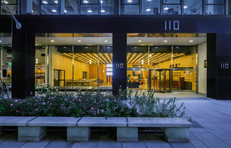 A window shows a yellow-lit building's lobby with plant life outside.