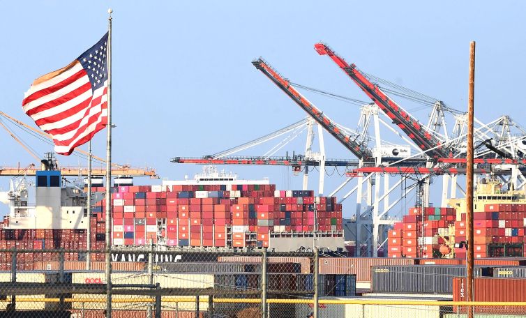 A US flag flies near containers stacked high on a cargo ship at the Port of Los Angeles on September 28 in Los Angeles. A record number of cargo ships are stuck floating and waiting off the southern California coast amid a supply chain crisis which could mean fewer gifts and toys for Christmas this year as a combination of growing volumes of cargo, Covid-19 related safety measures and a labor shortage slow the handling and processing of cargo from each ship.