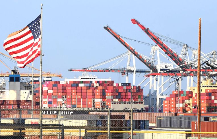 A US flag flies near containers stacked high on a cargo ship at the Port of Los Angeles on September 28 in Los Angeles. A record number of cargo ships are stuck floating and waiting off the southern California coast amid a supply chain crisis which could mean fewer gifts and toys for Christmas this year as a combination of growing volumes of cargo, Covid-19 related safety measures and a labor shortage slow the handling and processing of cargo from each ship.