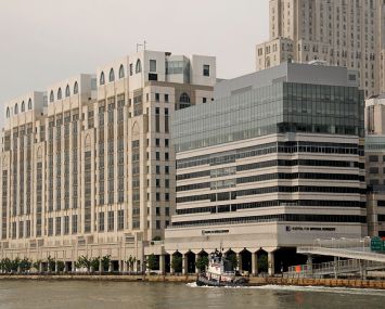 A large grey building with a glass top on a river as a boat passes.