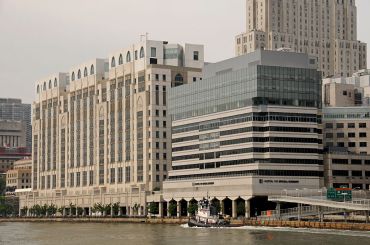 A large grey building with a glass top on a river as a boat passes.